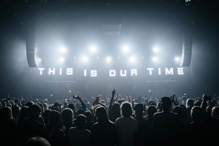 Crowd silhouetted against a wall of light reading This Is Our Time