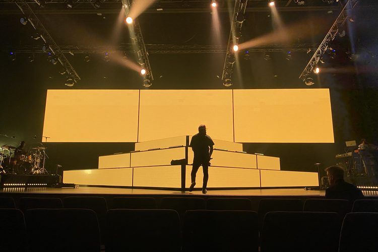 Stepped yellow set pieces with a single performer in silhouette