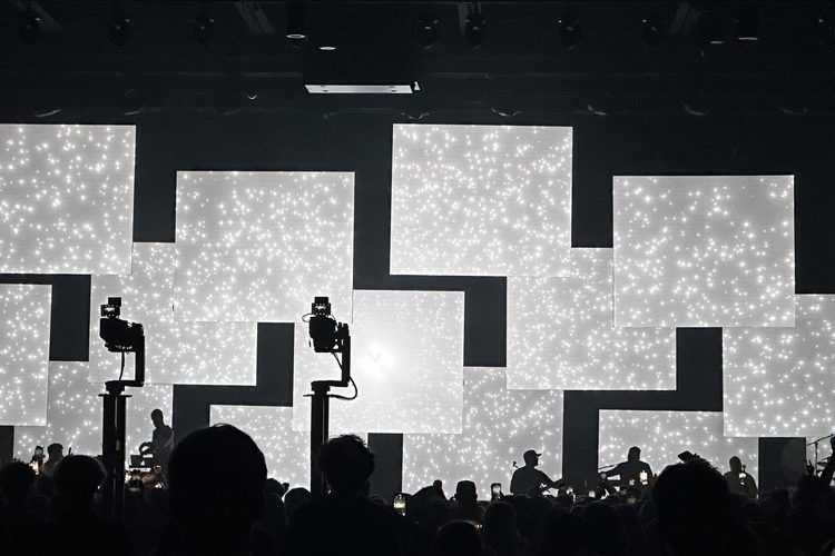 Monochrome tiled video wall behind a silhouetted crowd